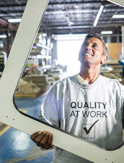 A man in a light-colored shirt holding a rectangular frame, smiling as he looks upwards, in an industrial workspace.