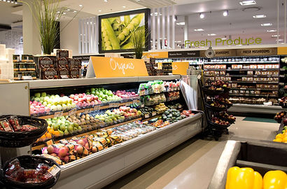 A grocery store produce section displaying various fruits and vegetables in organized displays, with signs for fresh produce in the background.